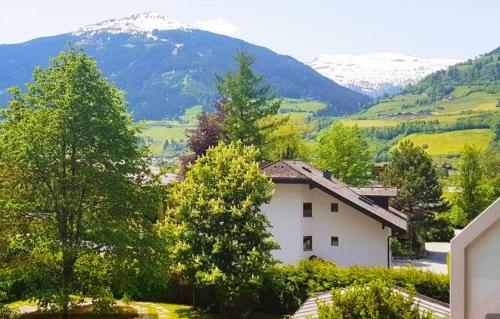 una casa blanca con árboles y montañas en el fondo en Alpenblick Apartment Gastein - inklusive Eintritt Alpentherme, en Bad Hofgastein