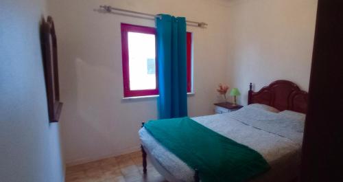 a bedroom with a bed with blue curtains and a window at Casa dos Buizinhos in Porto Covo