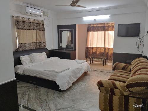 a bedroom with a bed and a couch and a tv at Sai Pavilion in Puttaparthi