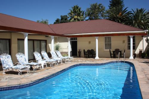 a swimming pool with chairs and a house at Karoopark Guest House in Graaff-Reinet