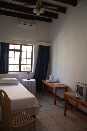 a bedroom with a bed and a table and a tv at Karoopark Guest House in Graaff-Reinet