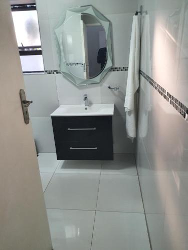Un baño blanco con lavabo y espejo. en Alu Guesthouse, en Roodepoort