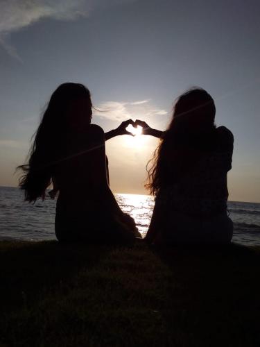 two women sitting on the beach with the sun in the background at HOSTAL BELLEZA TROPICAL in Moñitos