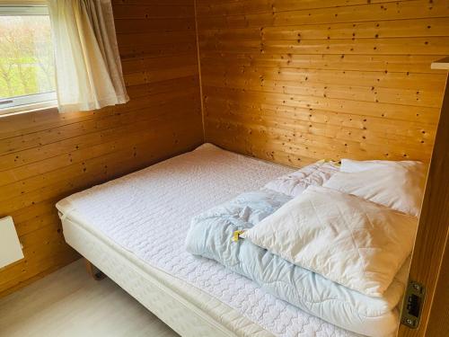 een leeg bed in een houten kamer met een raam bij Hummingen Camping hus 2 in Dannemare