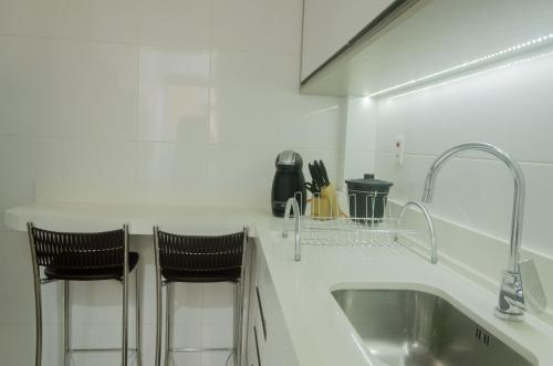 a white kitchen with a sink and two bar stools at No CENTRO de Cascavel, atras do Ibis, confortavel e bom gosto in Cascavel