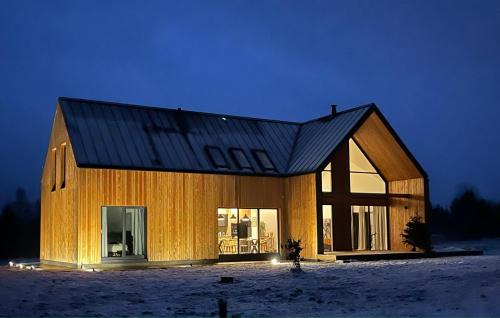 a wooden house with a black roof in the snow at TATANKA Dom w Puszczy & SPA na Polanie in Białowieża