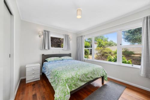 a bedroom with a bed and two windows at Blue Gate Cottage - Waikanae Beach Holiday Home in Waikanae