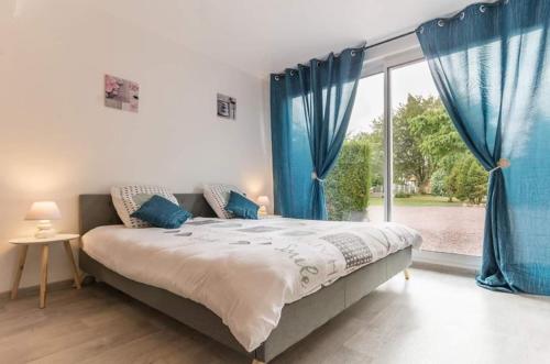 1 dormitorio con 1 cama con cortinas azules y ventana en Le studio du Pressoir, en Gisay