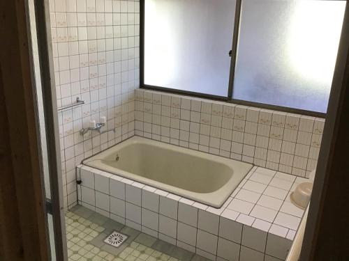 a bath tub in a white tiled bathroom at 富乃亭 in Maniwa