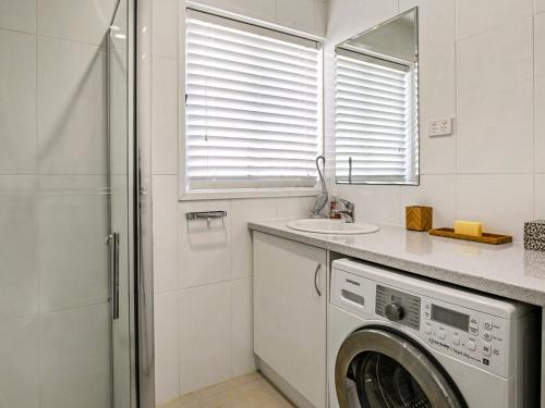 a washing machine in a white bathroom with a mirror at Gokus Shack Rural and water views with a spa in Corinella