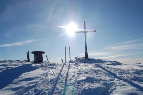 a cross on top of a snowy hill with the sun at Alpengasthof Krische in Murau