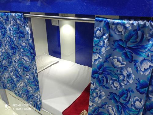 a small bed in a room with blue and white curtains at Kartar Yatri Niwas in Kānpur