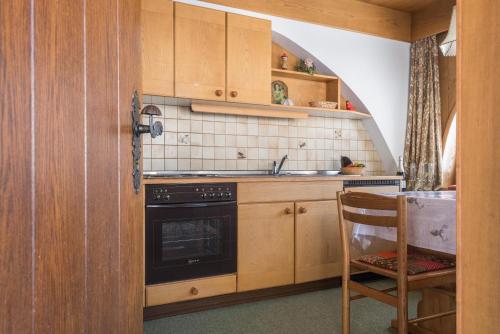 a kitchen with a stove and a sink and a chair at Kleine Gartenwohnung Haus Forelle in Selva di Val Gardena