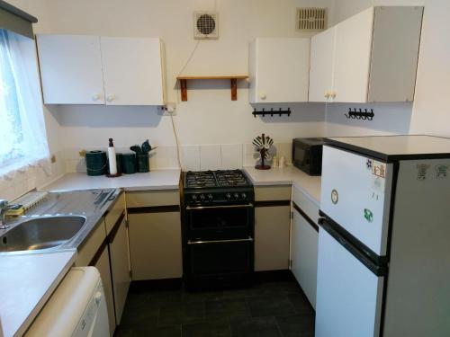 La cuisine est équipée de placards blancs et d'un four avec plaques de cuisson noires. dans l'établissement Wonderland Guest House, à Coventry