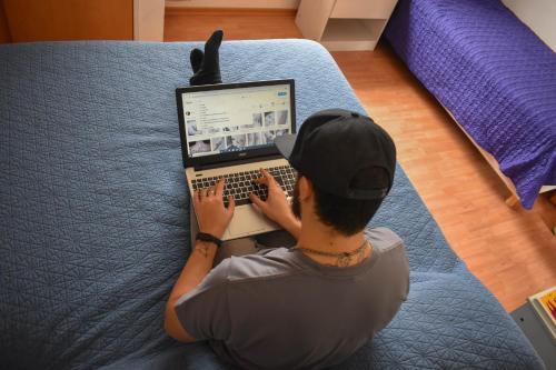 un hombre sentado en una cama usando un ordenador portátil en Complejo Solar Apart en Villa Regina