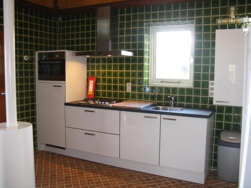 a kitchen with white cabinets and a sink and green tiles at vakantiehuis Warder in Warder
