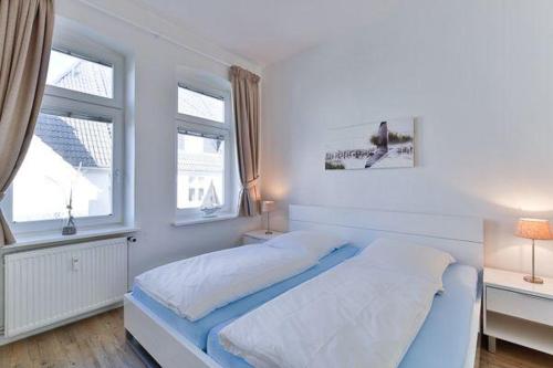 a white bedroom with a bed and two windows at App-6-mit-Suedbalkon-in-strandnaher-Lage-Baederstil-Villa-in-Wenningstedt-Sylt in Wenningstedt