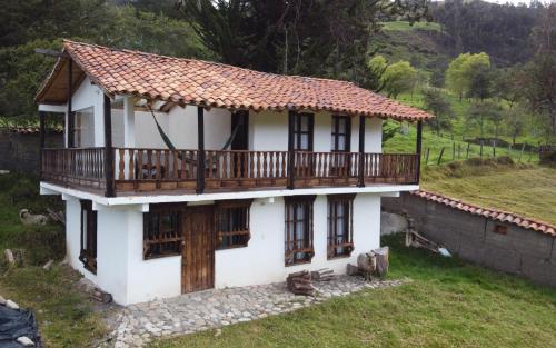 a small white house with a deck on a hill at La Posada Campestre Cabañas in El Cocuy