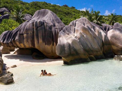 two people laying in the water on a beach with rocks at Raffles Seychelles in Baie Sainte Anne