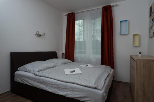 a bedroom with a bed and a window with red curtains at Lido Riviera Sunshine Apartman Balatonlelle in Balatonlelle