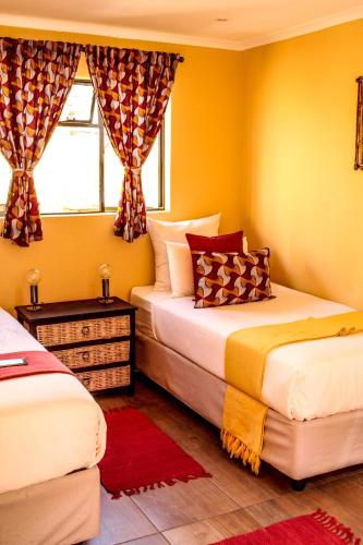 two beds in a room with yellow walls and a window at Lebo's Soweto Backpackers in Soweto