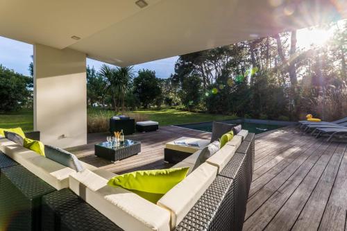 un patio extérieur avec des canapés et une terrasse en bois dans l'établissement OCTOPUS KEYWEEK Design villa on the Golf of Chiberta with heated pool, à Anglet