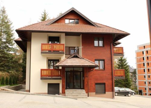 ein rotes Backsteingebäude mit Balkon und Dach in der Unterkunft Apartman Harmonija in Zlatibor