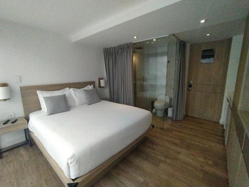 a bedroom with a large white bed and a bathroom at Urban Heights Bogota in Bogotá