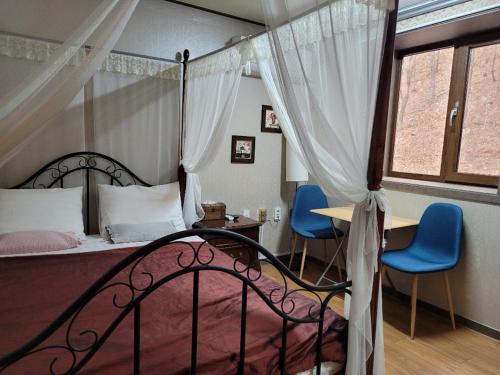 a bedroom with a canopy bed and two blue chairs at Sanaega Pension in Yangyang