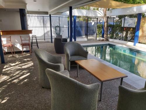 a swimming pool with chairs and a table next to a swimming pool at Cosmopolitan Motel & Serviced Apartments in Rockhampton