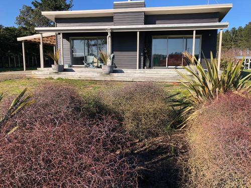 a house with a porch with bushes in front of it at Nikau’s on Palmer in Foxton Beach
