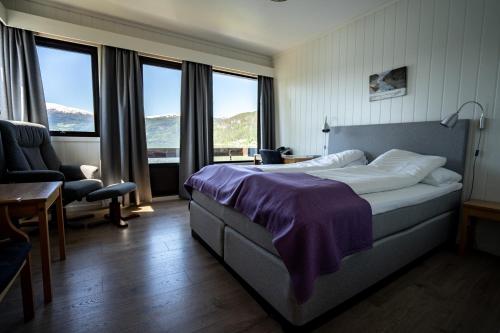 a bedroom with a bed and a chair and windows at Innvik Fjordhotell in Innvik