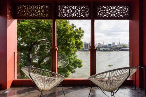 2 Stühle vor einem Fenster mit Flussblick in der Unterkunft Amdaeng Bangkok Riverside Hotel - SHA Plus Certified in Bangkok