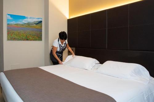 Una donna sta facendo un letto in una camera da letto di City Hotel & Suites a Foligno