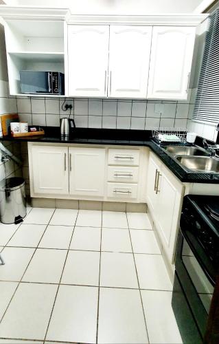 a kitchen with white cabinets and a white tile floor at Laboria 102 & 103 in Harrismith