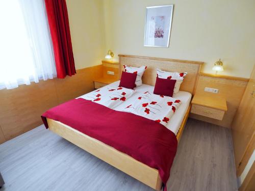 a bedroom with a large bed with red sheets and red pillows at Pension Kathi in Sankt Kanzian