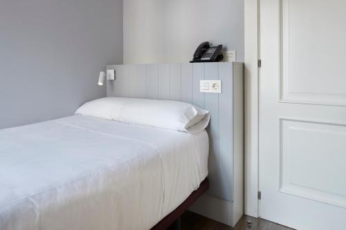 
a white bed in a bedroom next to a wall at Hotel Avenida in Pamplona
