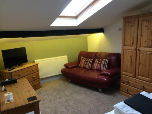 a living room with a brown leather couch and a television at Burcott Mill Guesthouse in Wells