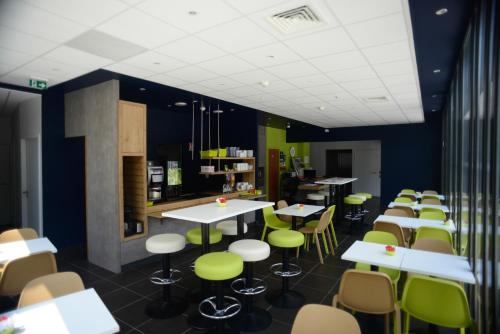 um restaurante com mesas brancas e cadeiras verdes em ibis budget Gare de Poitiers em Poitiers