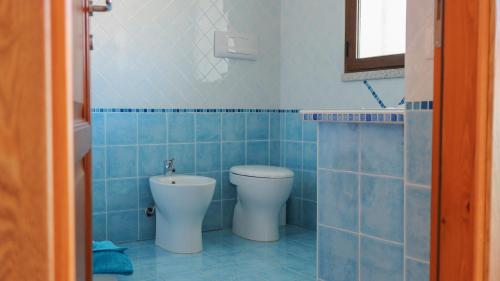 Un baño con azulejos azules, inodoro y lavabo. en Baia, en Budoni