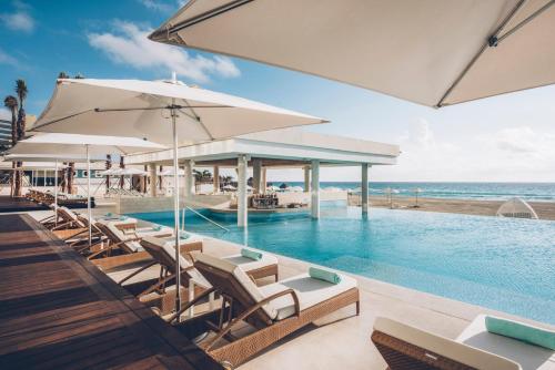 a pool with chairs and umbrellas next to the ocean at Iberostar Selection Coral Cancun - Adults Only All Inclusive Resort in Cancún