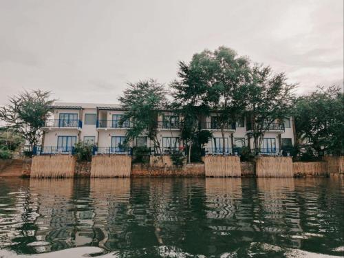 a white building with trees in front of the water at The B Resort in Kampot