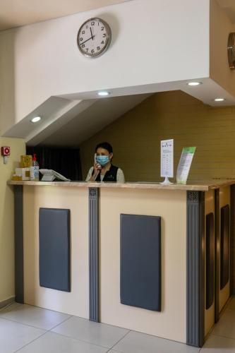 a man wearing a mask behind a counter with a clock at 7 days hotel in Almaty