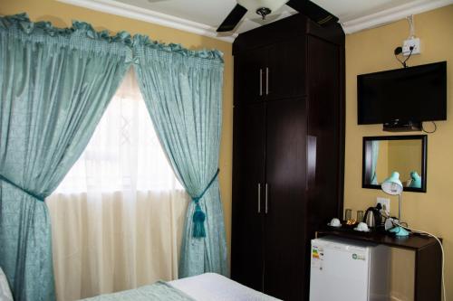 a bedroom with a window with blue curtains and a refrigerator at Mrhali Boutique Guest House in Kwamhlanga