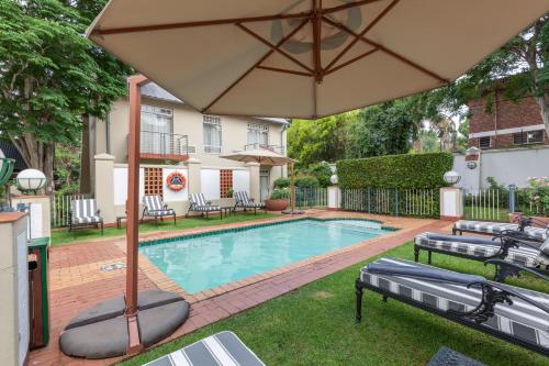 a swimming pool with a large umbrella and chairs at Courtyard Hotel Arcadia in Pretoria