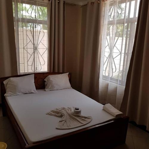 a bed in a bedroom with two windows at Prideinn Lodge Kigamboni in Dar es Salaam