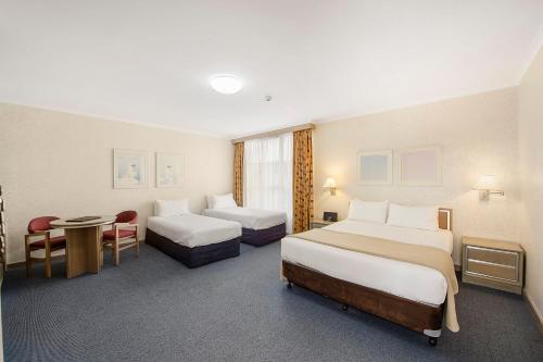 a hotel room with two beds and a table at Mid City Motel Warrnambool in Warrnambool