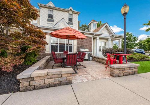 a patio with red chairs and a table with an umbrella at Birch Hills Suites - Blue Ash in Blue Ash