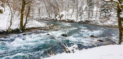 a stream with snow on the ground next to a river at Domacinstvo na kraju svijeta in Šipovo