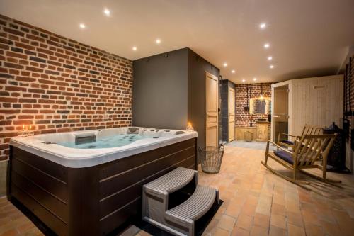 a large bath tub in a room with a brick wall at Le Pigeonnier, maison d'hôtes et Spa in Croix